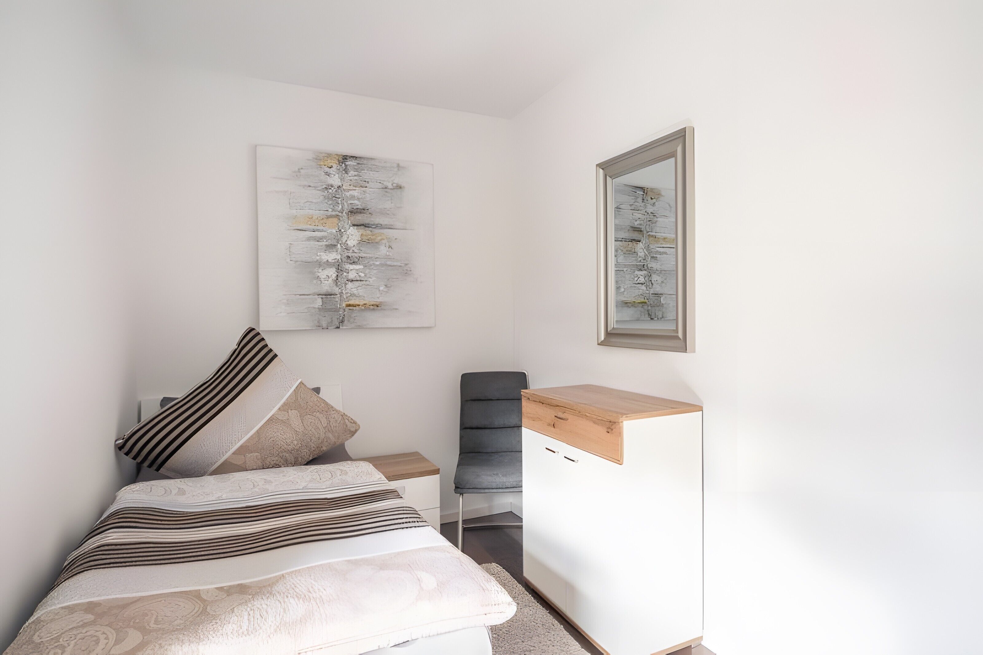 Un dormitorio con cama, escritorio, silla, armario y dos obras de arte en la pared.
