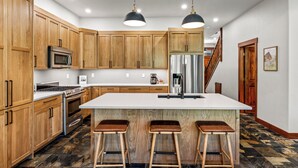 A modern kitchen with wooden cabinets, a stainless steel refrigerator, a large island with stools, and a patterned tile floor.