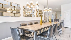 A modern dining area with a long wooden table, black leather chairs, and a decorative gold vase. - Luxury Home with Private Pool in Kissimmee (Kissimmee)