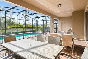 Un espace extérieur abrité doté d’une piscine, de meubles en osier et d’une structure en verre.