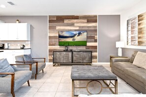 A modern living room with a flat-screen TV, grey upholstered sofas, a grey ottoman, and a wooden cabinet.