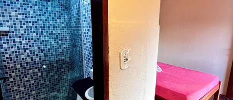 A bathroom with a toilet, a shower area with blue mosaic tiles, and a wooden bench with a pink towel.