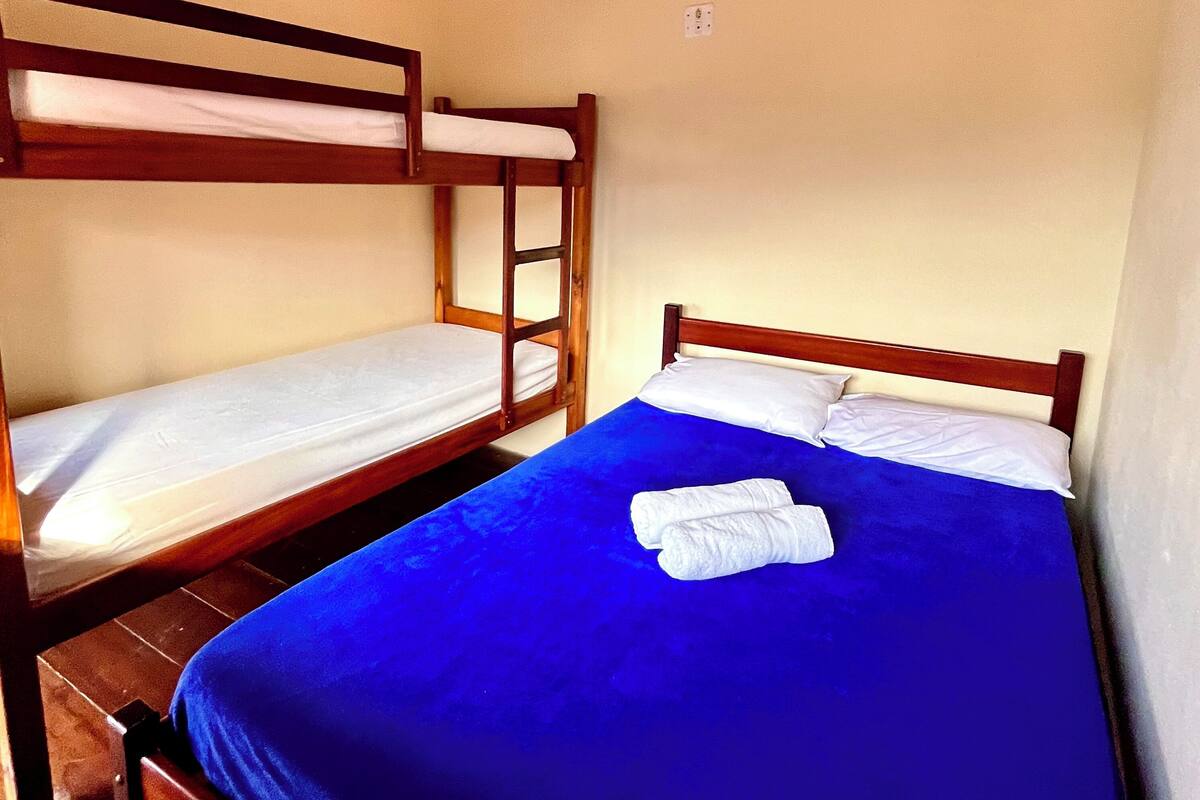 Une chambre avec deux lits superposés, l’un avec une structure en bois et l’autre avec une structure en métal, et les deux sont équipés de draps blancs.