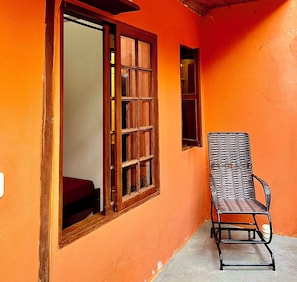 A room with a wooden-framed window, a wicker chair, and an orange wall. - Pouso Paraty (Paraty)