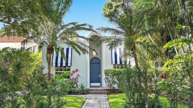 A house with a blue door, surrounded by lush greenery and a stone pathway leading to the entrance.