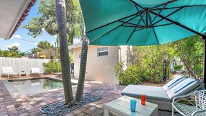 A poolside area with a lounge chair, a table, and an umbrella.