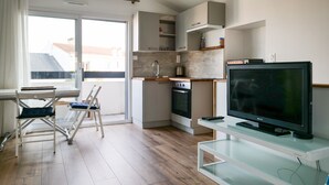 Une cuisine moderne dotée d’un four encastré, un coin repas avec une table et des chaises, et un grand téléviseur à écran plat posé sur un meuble.