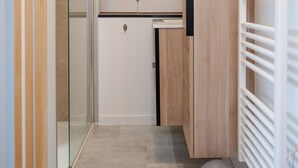 Un couloir étroit avec une porte vitrée, un petit coin cuisine doté de meubles en bois et un radiateur sur le côté droit.