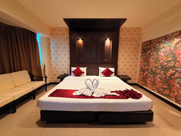 A hotel room with a large bed, a sofa, a nightstand, and a floral wallpaper.