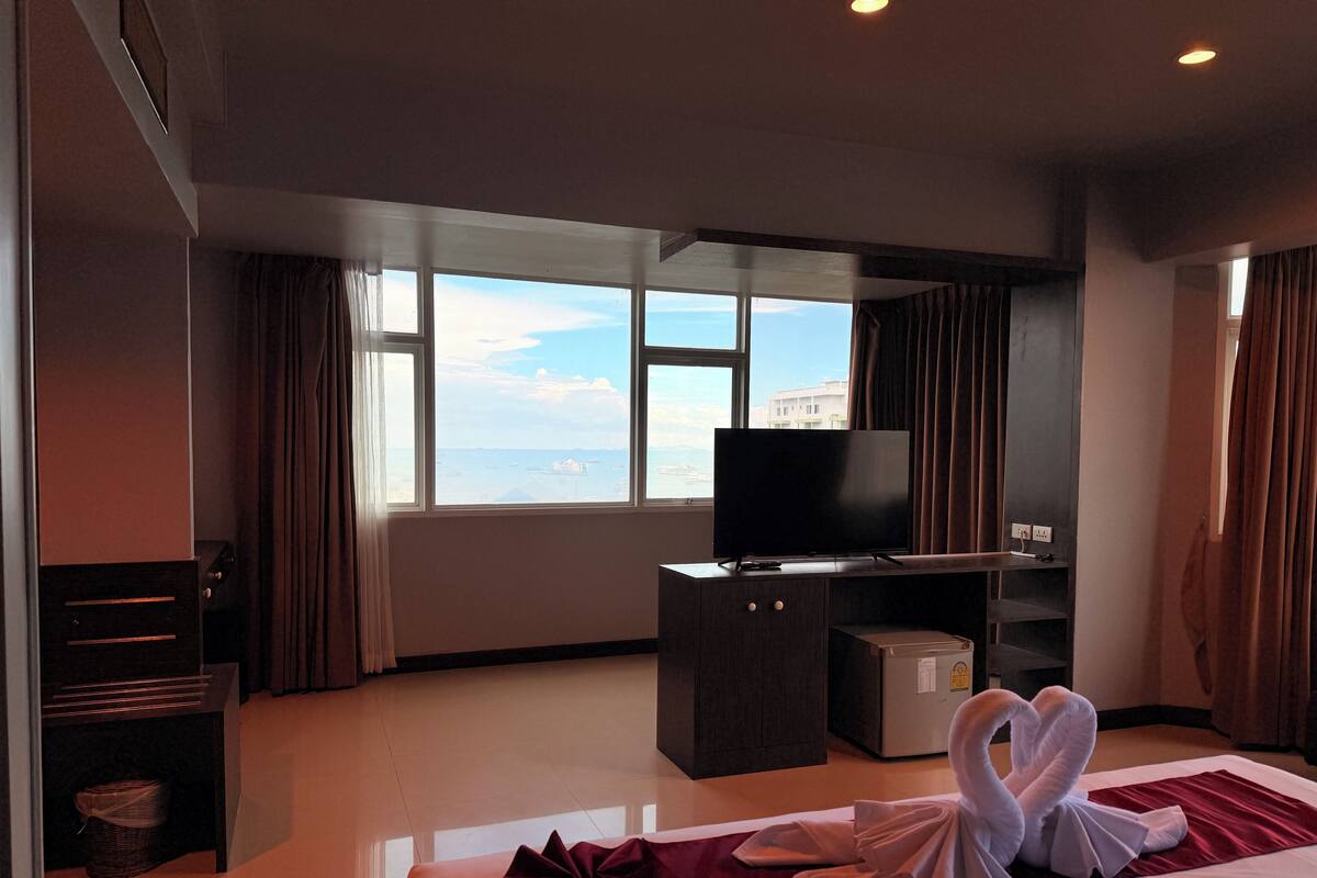 A hotel room with a bed, a TV, a desk, and a view of the sea.