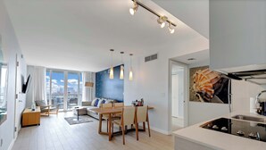 A modern kitchen with a central island, a dining area with a wooden table and chairs, and a living room with a sofa and a TV.