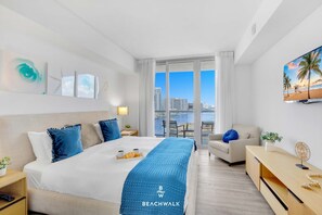 A hotel room with a bed, a desk, a chair, a TV, and a balcony with a city view.