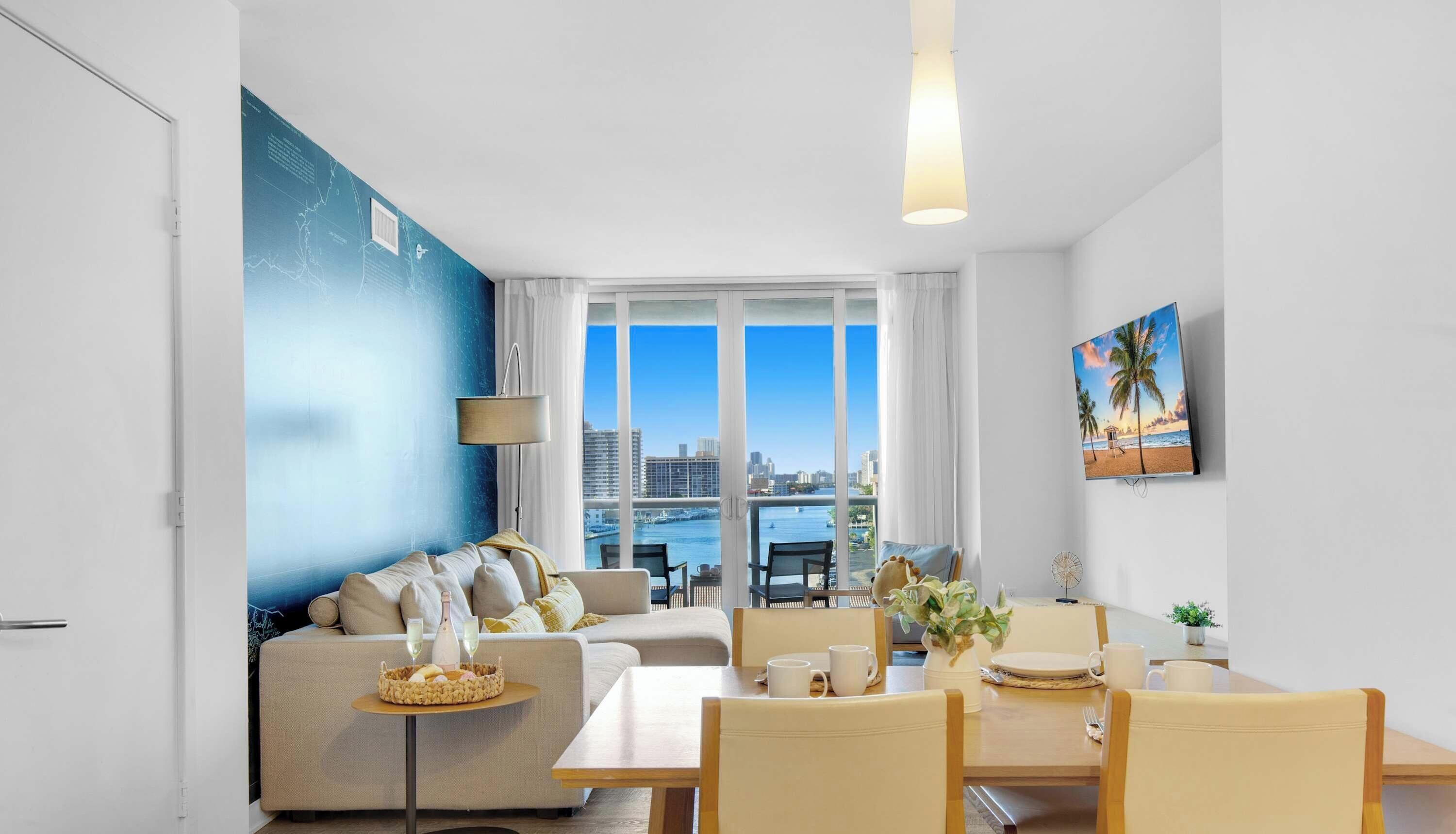 A modern living room with a sofa, dining table, chairs, and a city view through large windows.