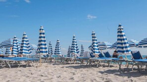 A beach with striped umbrellas and lounge chairs.