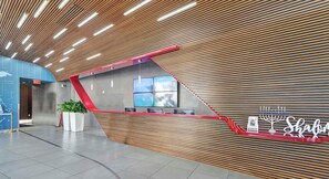 A modern reception area with a sloped ceiling, a reception desk, a digital screen, and a wall-mounted menorah.