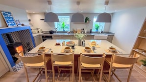 Una cocina moderna con una isla central, sillas de madera, iluminación colgante y una estufa a la vista.