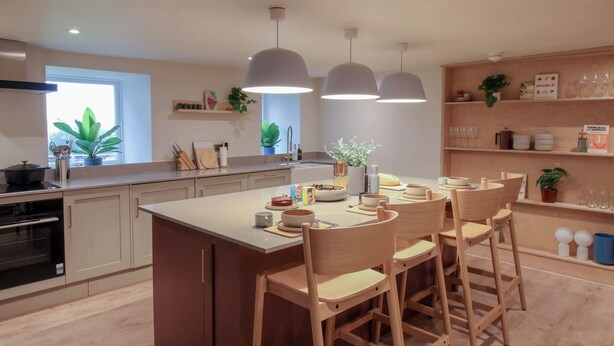 Una cocina moderna con una isla central, sillas de madera, iluminación colgante y vistas al exterior.