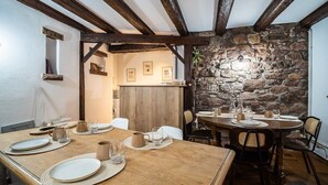 Un coin repas agrémenté d’un mur en pierre rustique, de poutres en bois et d’une table en bois dressée pour quatre personnes.