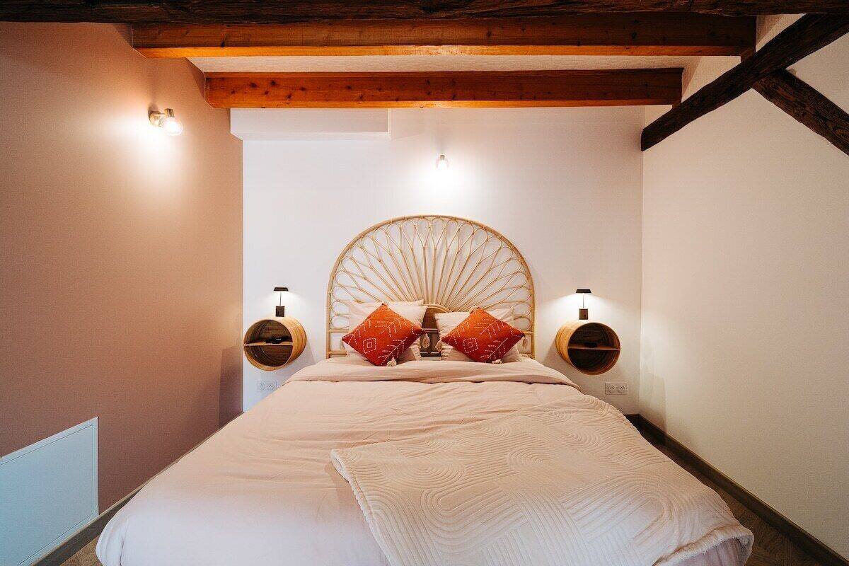 Une chambre à coucher avec un grand lit, deux lampes fixées au mur et une poutre en bois au plafond.