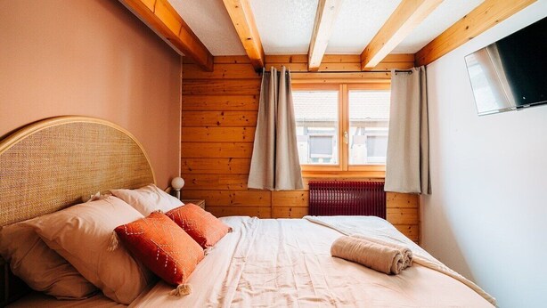Une chambre confortable avec une tête de lit en bois, un grand lit avec une literie beige et une fenêtre avec des rideaux.