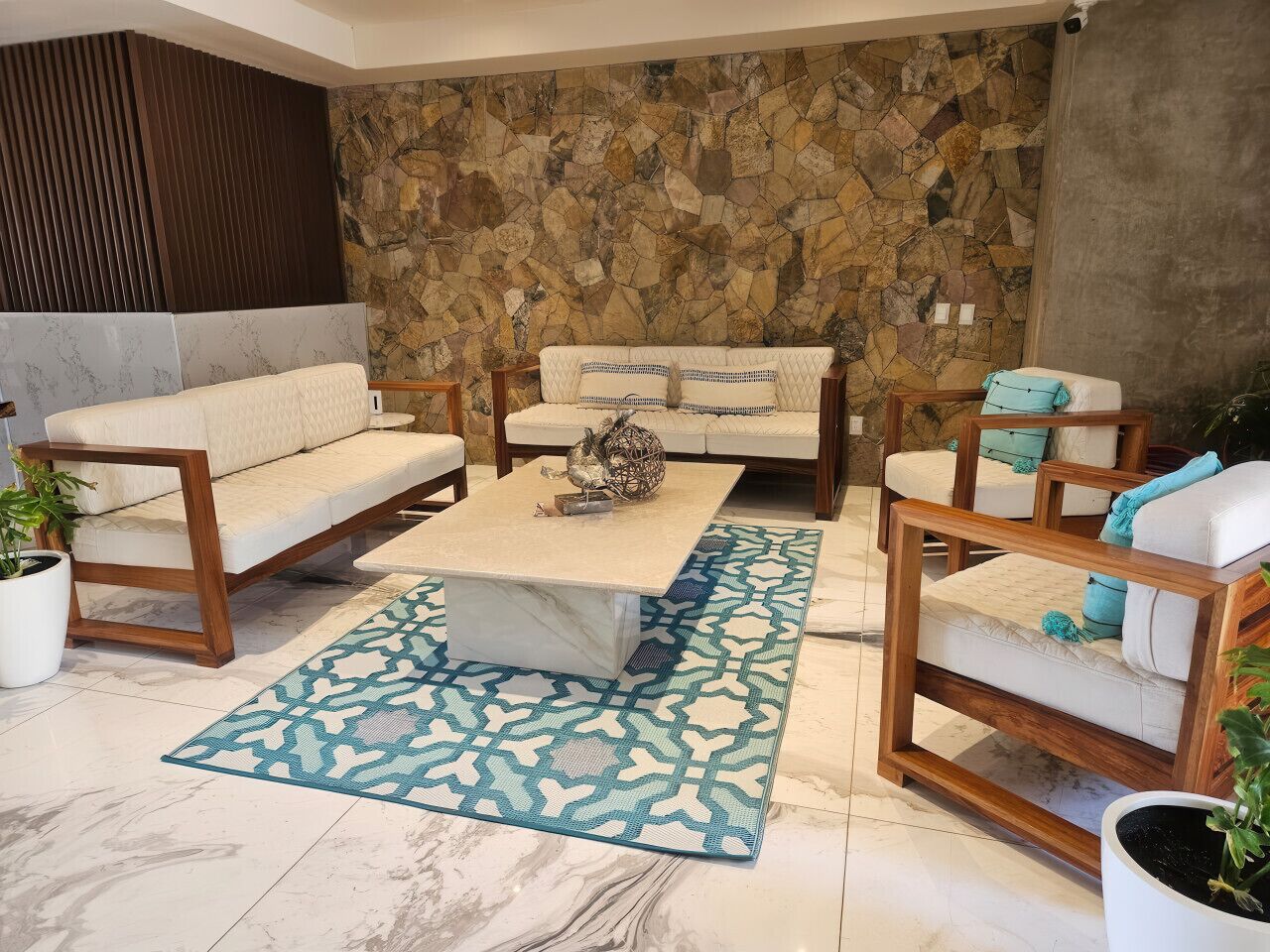 A living room with a stone wall, a sofa set, a coffee table, and patterned rugs.