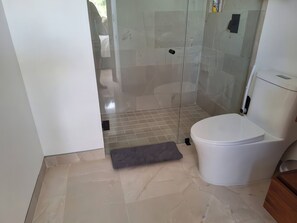 Een badkamer met een glazen douchecabine, een wit toilet en een klein vloerkleed.