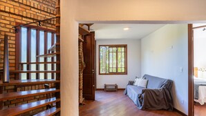 A room with a wooden staircase, a window with a view of greenery, a grey sofa, and a small table. - House With BBQ 550m From the Beach Gss0488 (Florianópolis)