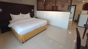 Une chambre d’hôtel moderne dotée d’un grand lit, d’une tête de lit en bois, d’un élément de séparation décoratif et d’un coin cuisine.