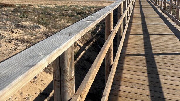 A wooden boardwalk leading to a beach with a clear blue sky.