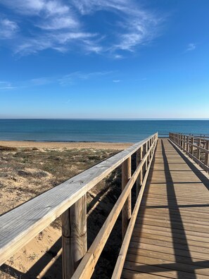 Une promenade en bois qui mène à une plage, avec un ciel bleu dégagé.