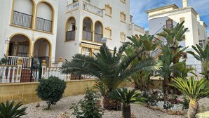 A multi-story building with balconies, arched doorways, and a garden with palm trees.