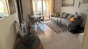 A living room with a sofa, a dining table with chairs, a ceiling fan, and a view through a glass door to an outdoor area.