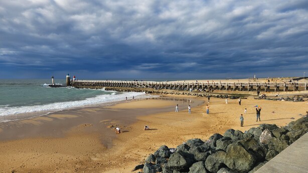 A beach with a rocky breakwater, a lighthouse, and a sandy shore.