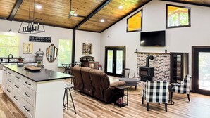 Amplia sala de estar con techo de madera, chimenea, televisor grande y un rincón de estar acogedor.