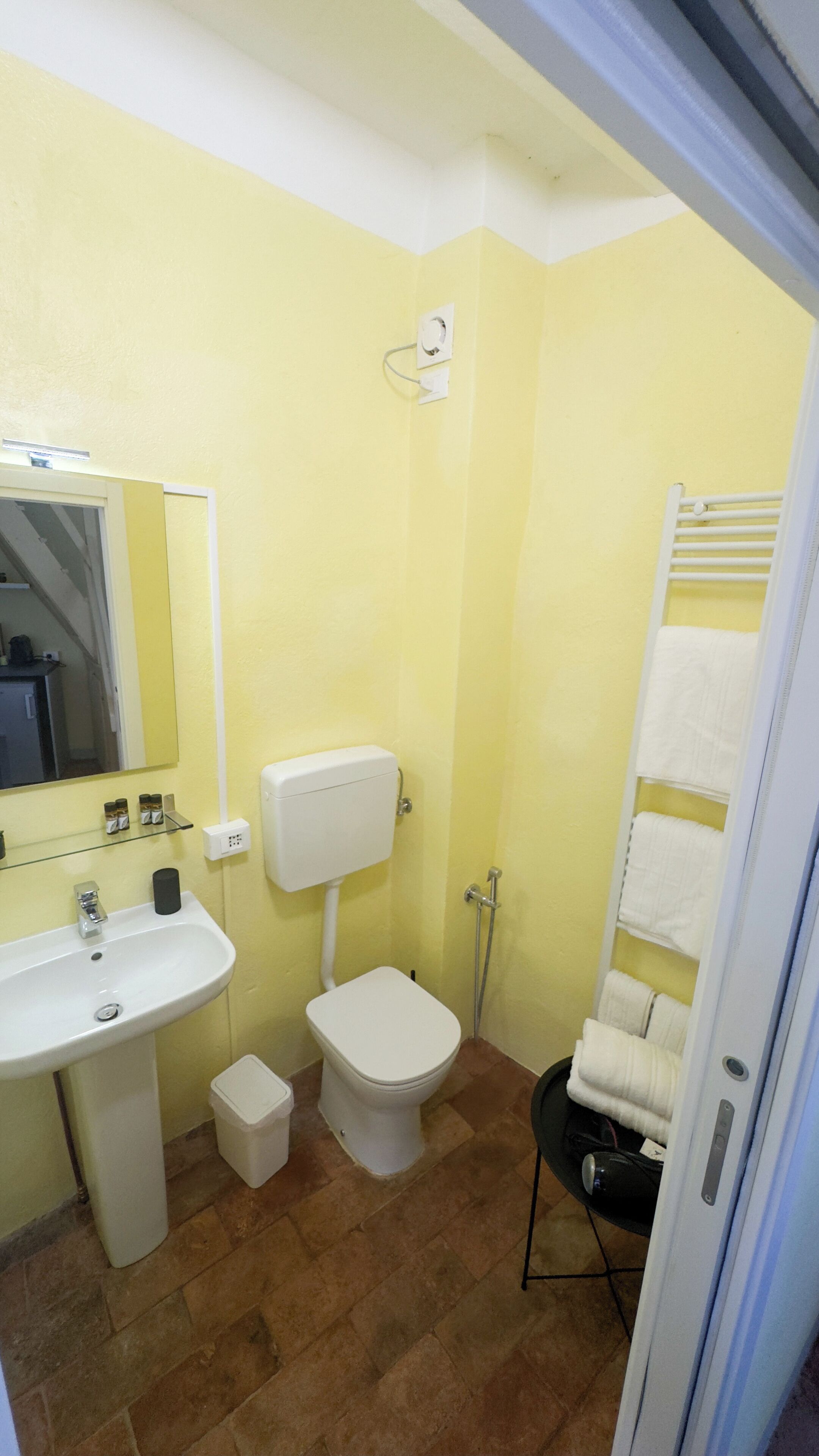 A bathroom with a yellow wall, white sink, toilet, and a towel rack.