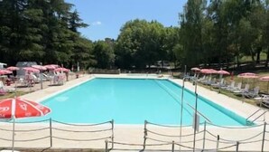 A rectangular swimming pool with a fenced area, surrounded by trees and equipped with sun umbrellas and lounge chairs. - Residenze del borgo (Zavattarello)