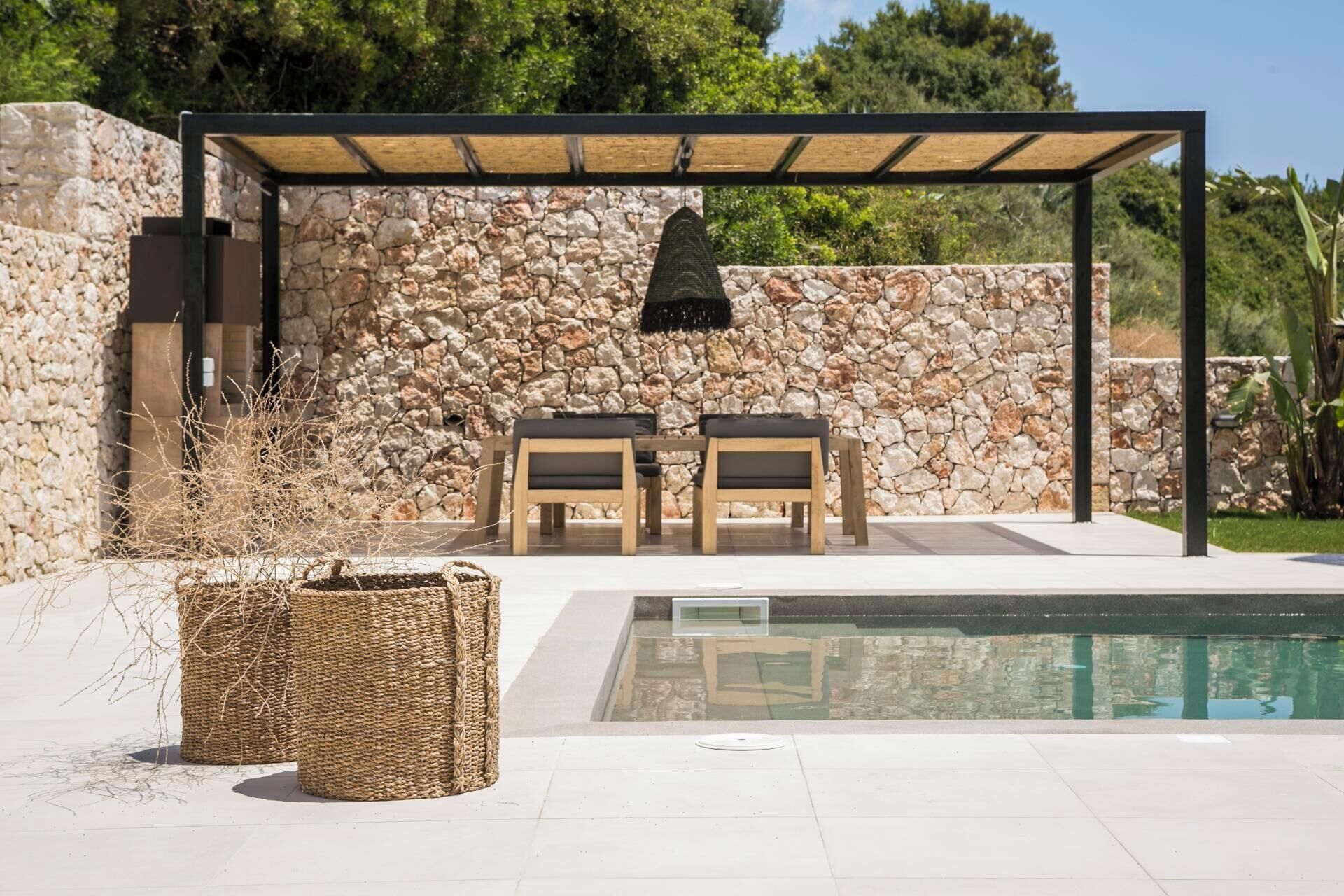 Un espacio de estar al aire libre cubierto con un fondo de pared de piedra, una piscina y una cesta tejida.