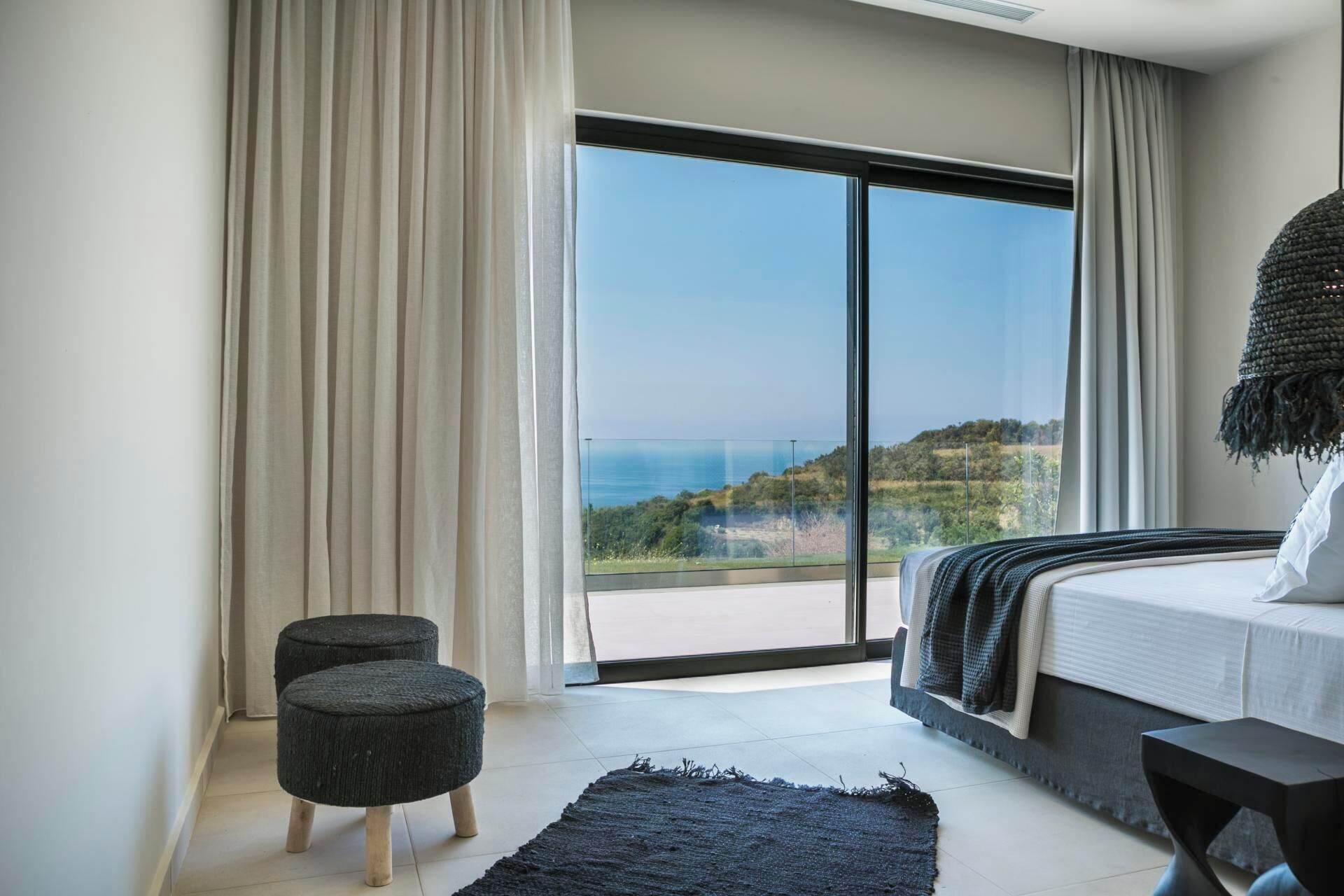 A modern bedroom with a large sliding glass door leading to a balcony with a scenic view.