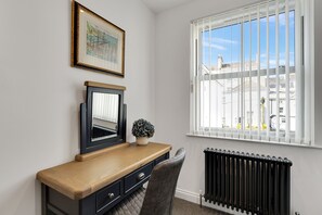 A room with a wooden desk, a chair, a radiator, a window with blinds, and a framed picture on the wall.
