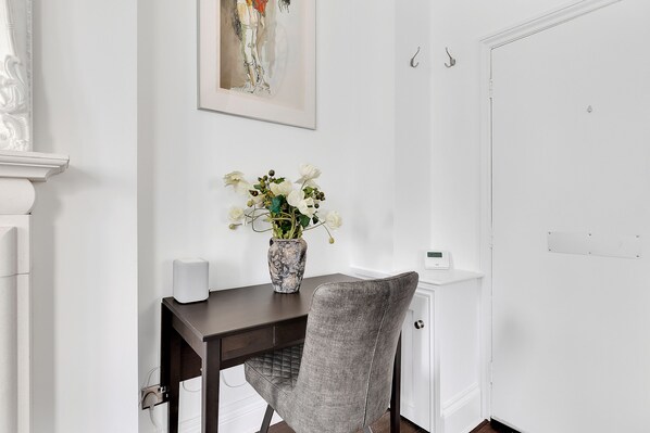 A dining area with a dark wooden table, a grey upholstered chair, a vase with white flowers, and a framed artwork on the wall.