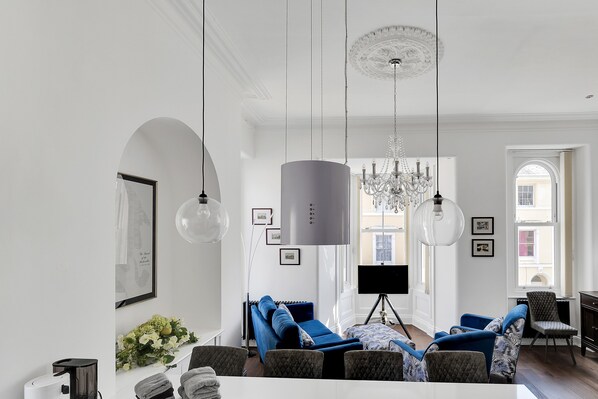 A modern living room with a sofa set, a chandelier, and a flat-screen TV.