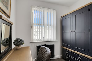 A room with a large wardrobe, a radiator, a potted plant, and a window with blinds.