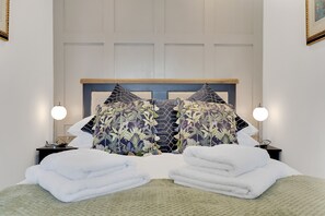 A neatly made bed with white towels, a headboard with a geometric pattern, and two bedside lamps.