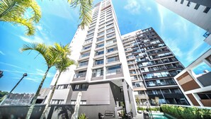 A high-rise building with multiple balconies, a swimming pool, and palm trees.