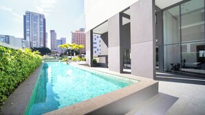 A modern building with a swimming pool, large windows, and a view of tall buildings in the background.