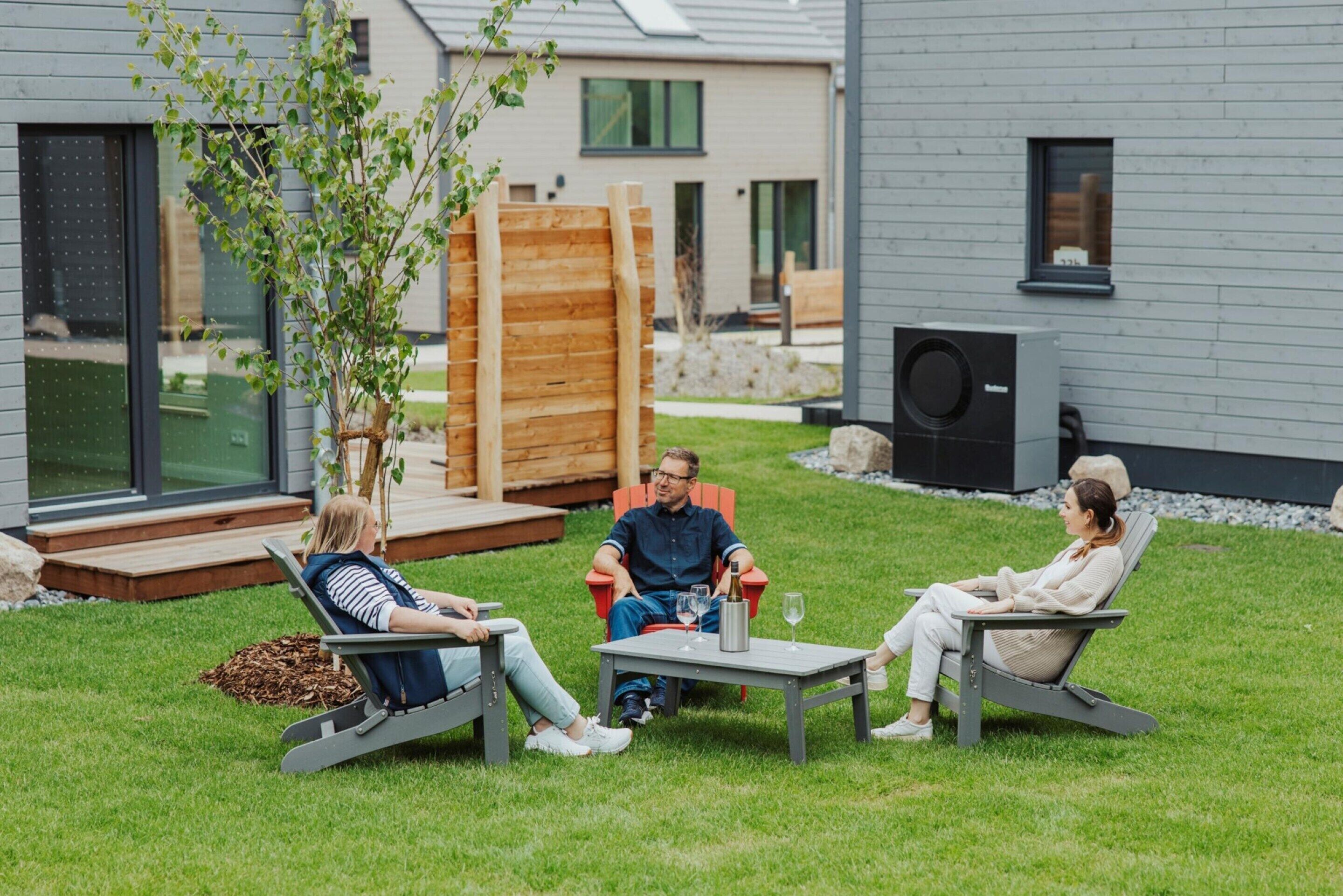 Three people seated on outdoor furniture in a modern outdoor setting with a wooden deck and a building in the background.