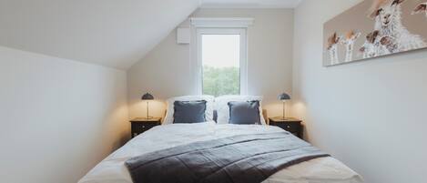 A bedroom with a large bed, two bedside tables, a window, and a wall-mounted painting.