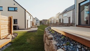 A modern residential area with a narrow pathway flanked by houses with large windows and a wooden deck. - Skandinavisch Eingerichtetes Familienferienhaus (Sagard)