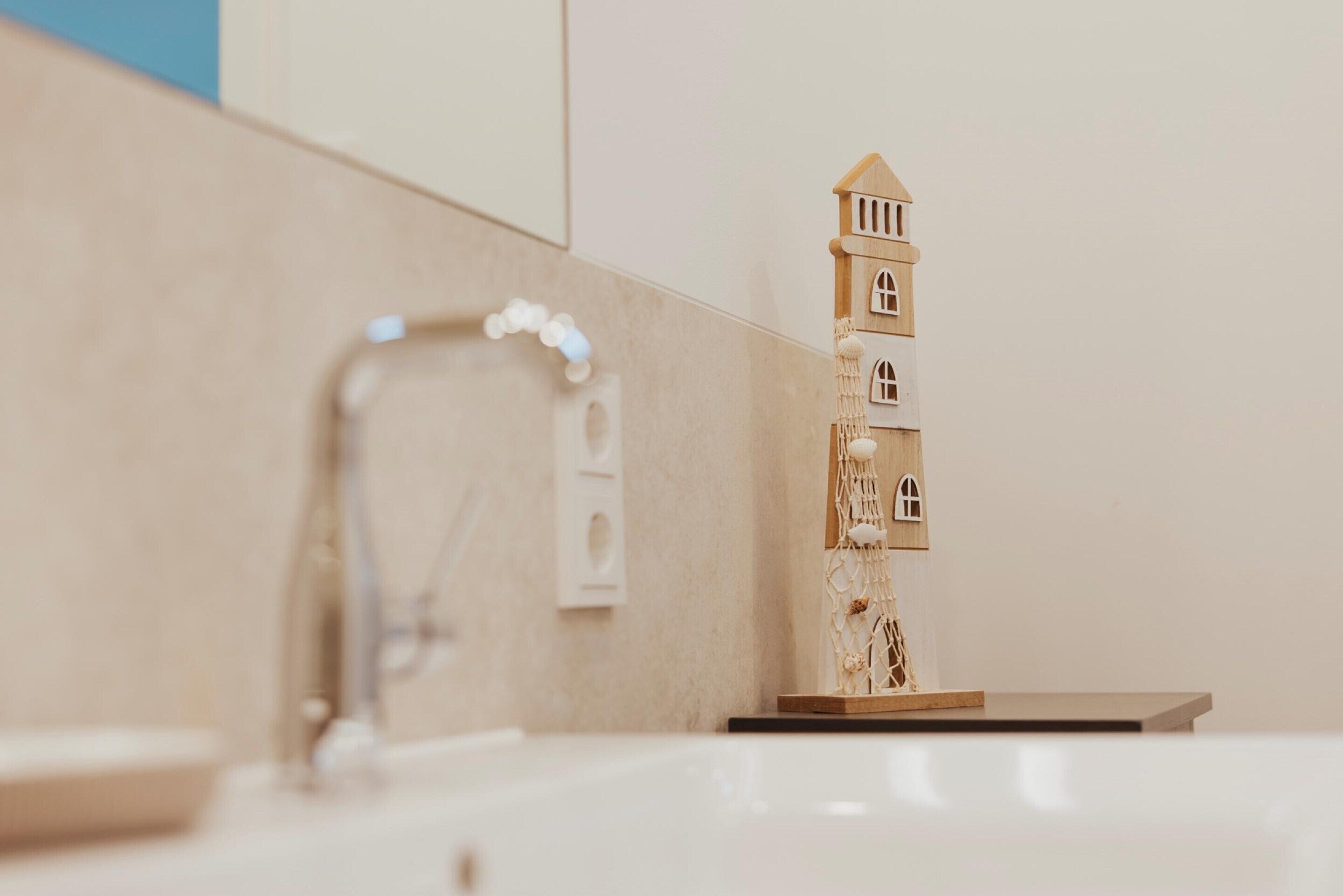 Une salle de bain avec une maquette de maison en bois, un robinet et un miroir.