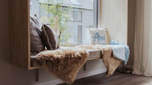 A cozy seating area with a fur throw, pillows, and a window with a view of a house and tree. - Skandinavisch Eingerichtetes Familienferienhaus (Sagard)